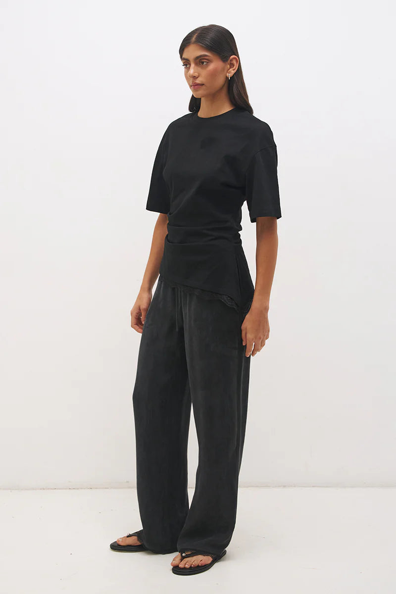 Mon Renn Liora T-Shirt in Black — three-quarter side view showing cinched waist seaming, angled lace hem and asymmetric side split