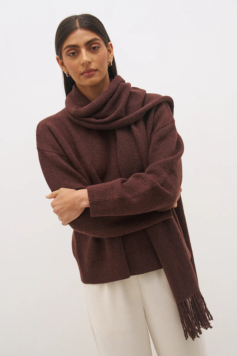 Mon Renn Scarf Knit Jumper in Cacao — cropped upper body shot, arms crossed with scarf wrapped high showing fringe tassels and ribbed cuffs