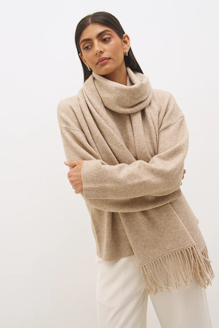Mon Renn Scarf Knit Jumper in Natural — cropped upper body shot, arms crossed with scarf wrapped high showing fringe tassels and ribbed cuffs